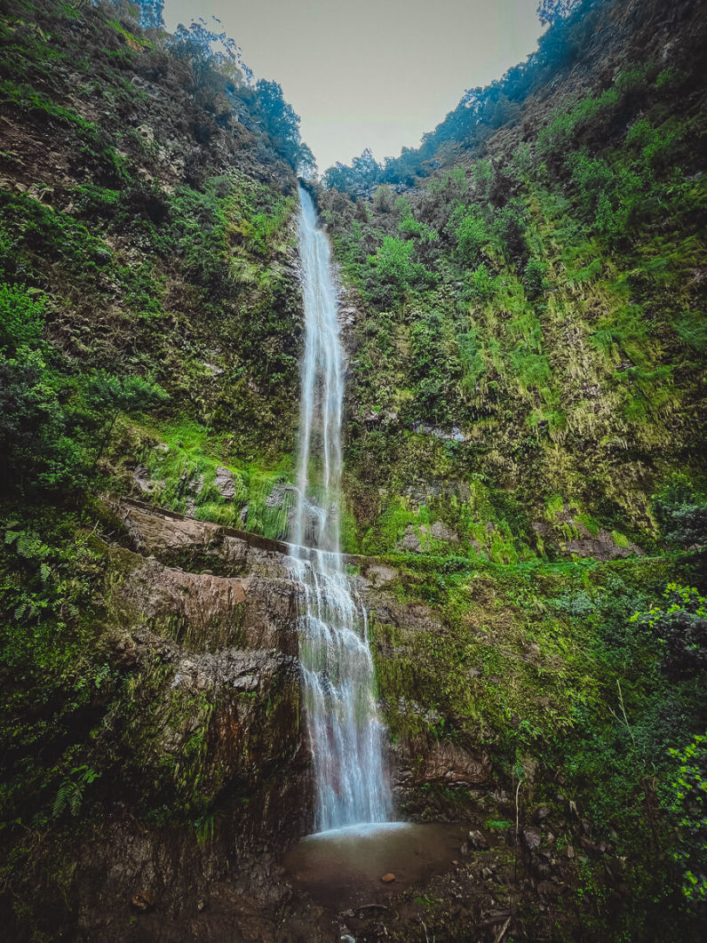 A massive waterfall dropping from a high cliff surrounded by green nature